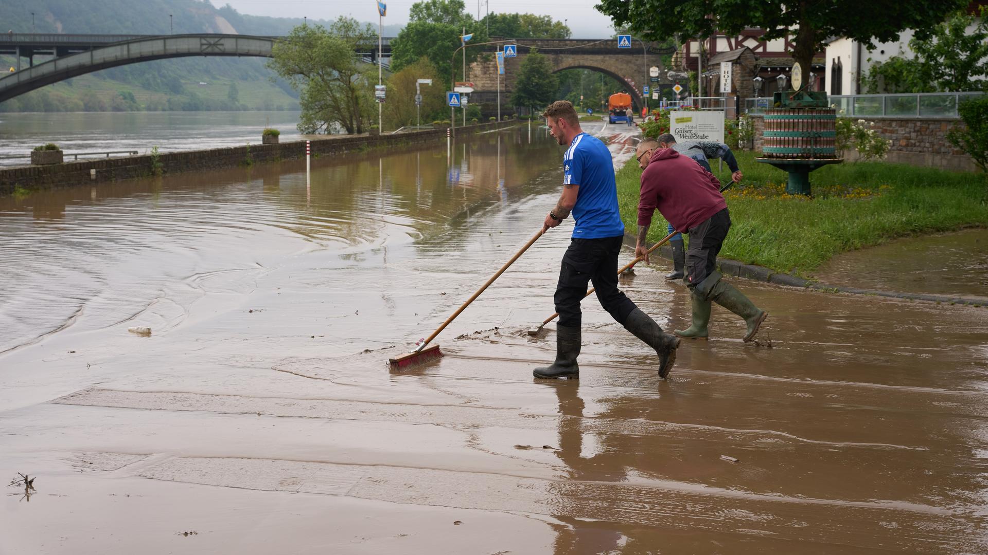 Mehrere Männer schieben mit Besen Wasser von einer Straße.