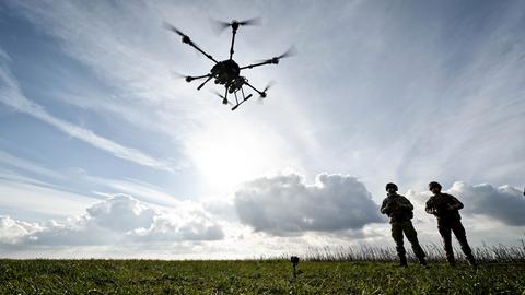 Zwei Soldaten stehen im Gegenlicht auf einem freien Feld, während über ihnen eine Drohne schwebt.