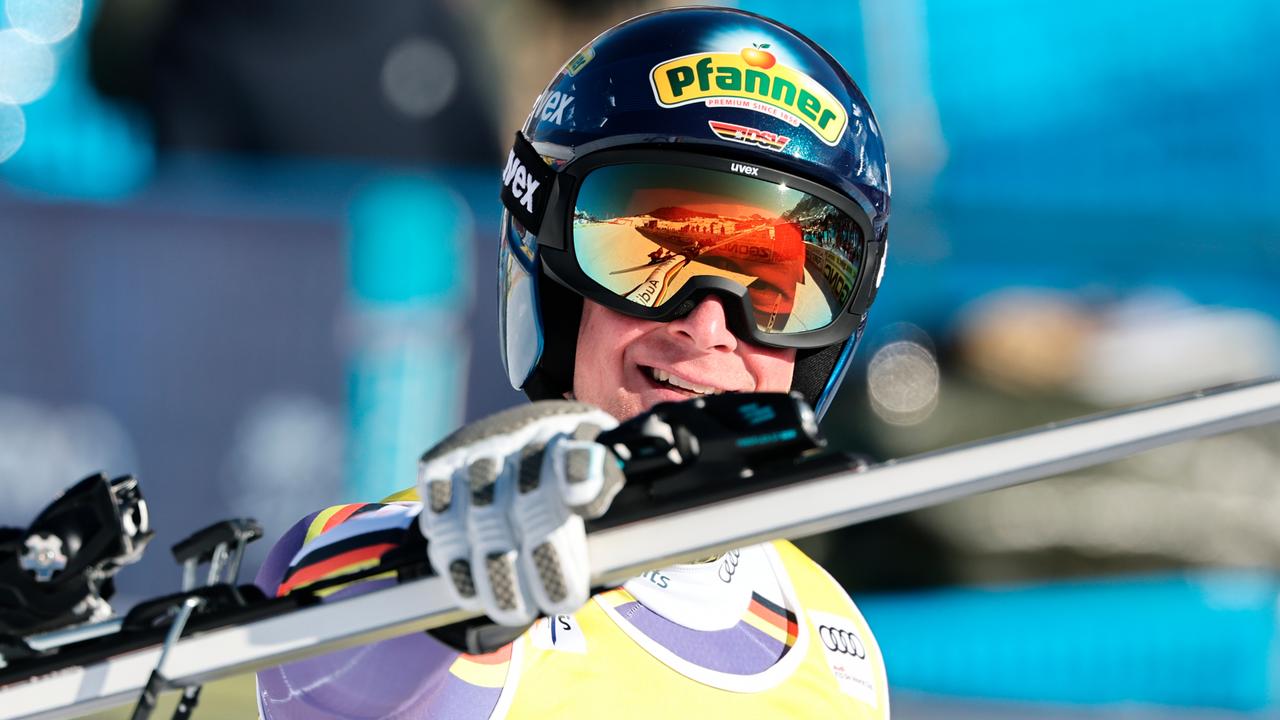 Man sieht den Oberkörper des lachenden Jocher mit Helm und Skibrille. Er hält einen Ski hoch und deutet mit dem Zeigefinfer in Richtung des Betrachters. 