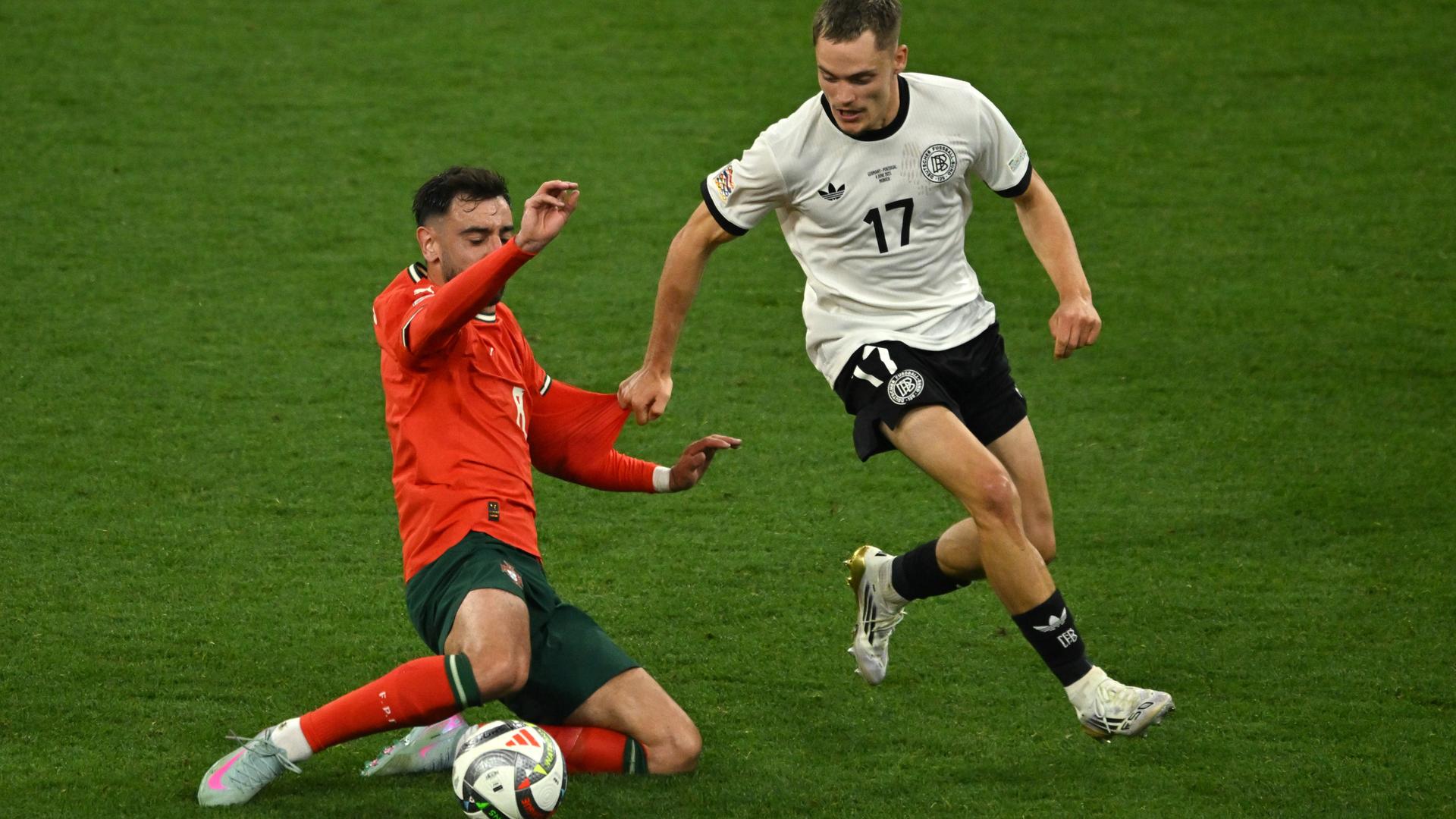 Das Bild zeigt Bruno Fernandes und Florian Wirtz, die auf dem Platz engagiert um den Ball kämpfen. Das Bild zeigt Bruno Fernandes und Florian Wirtz, die auf dem Platz engagiert um den Ball kämpfen.