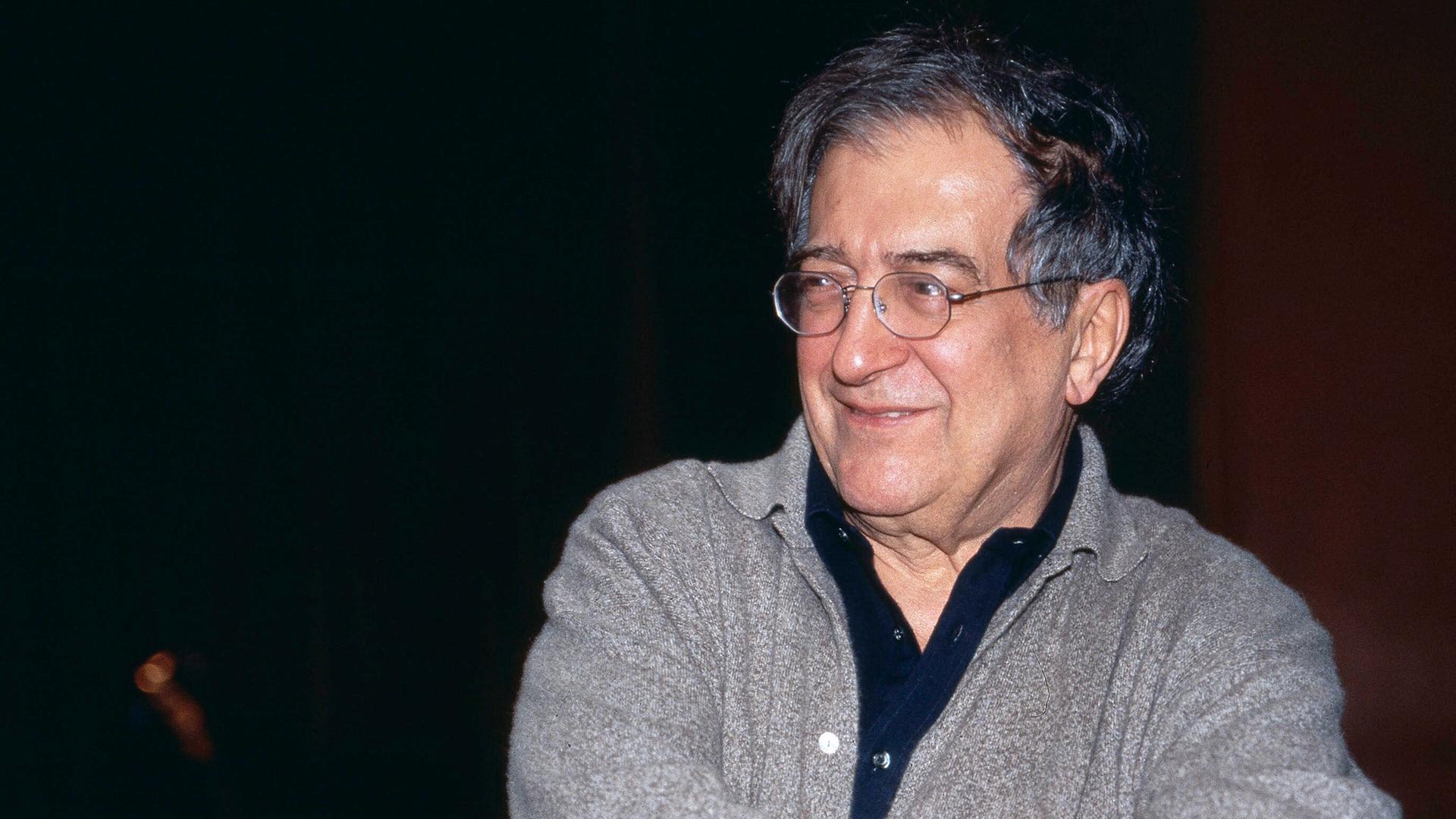 Luciano Berio sitzt in grauer Strickjacke und mit Brille in einer Opernprobe und lacht seitlich an der Kamera vorbei. Luciano Berio sitzt in grauer Strickjacke und mit Brille in einer Opernprobe und lacht seitlich an der Kamera vorbei.