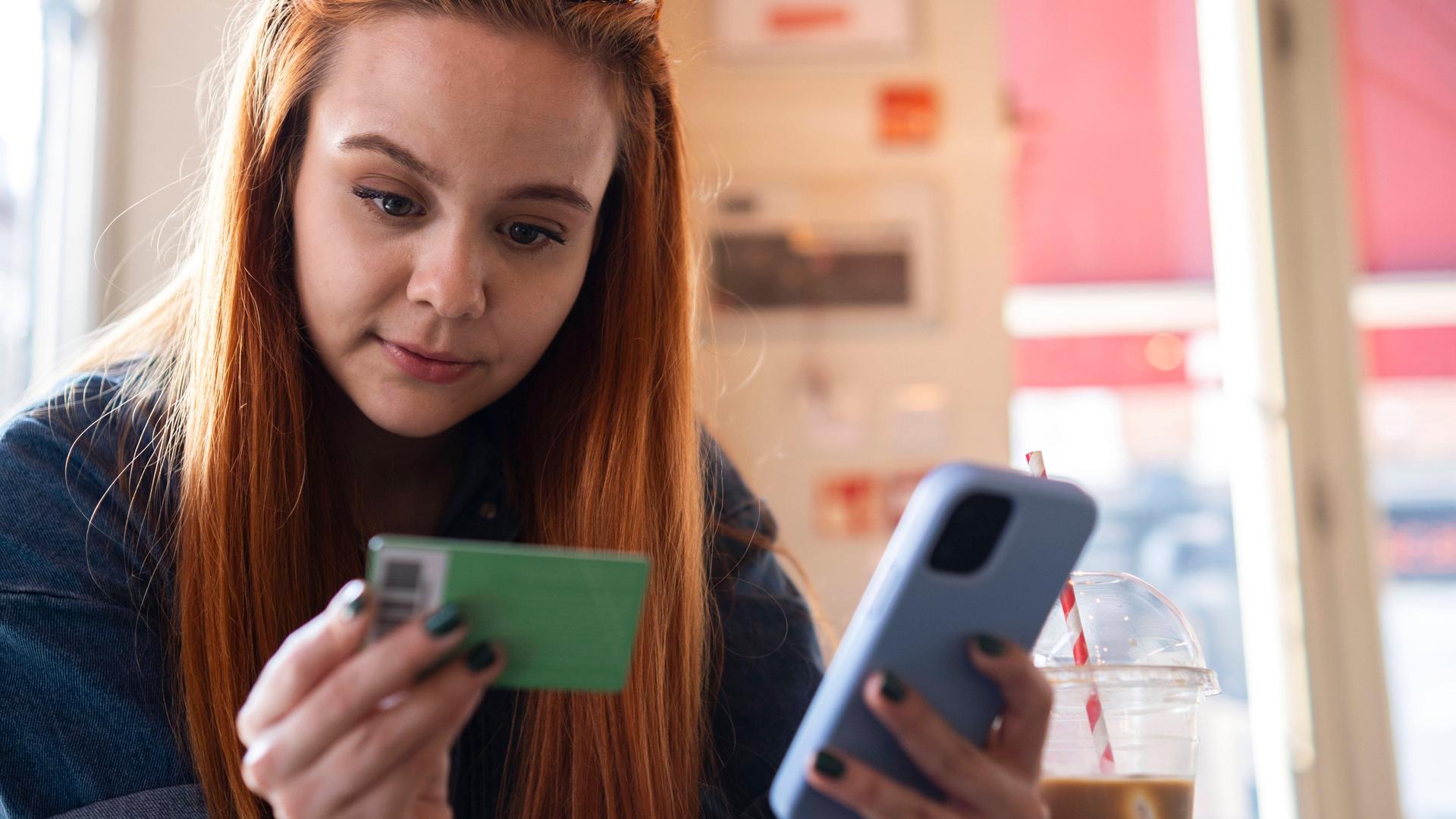 Eine Frau hält ein Smartphone und eine Bankkarte in er Hand. 