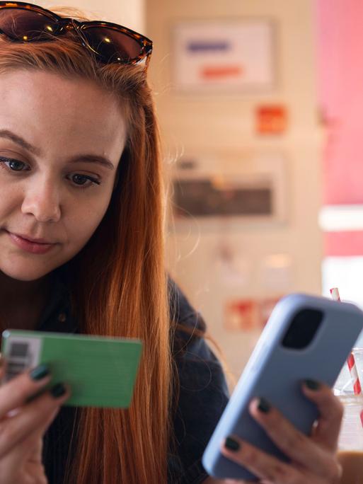 Eine Frau hält ein Smartphone und eine Bankkarte in er Hand. 