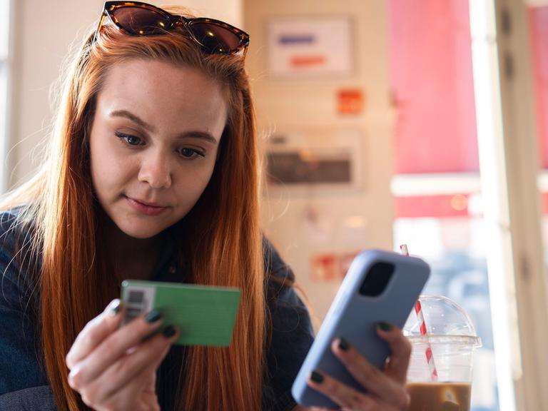 Eine Frau hält ein Smartphone und eine Bankkarte in er Hand. 