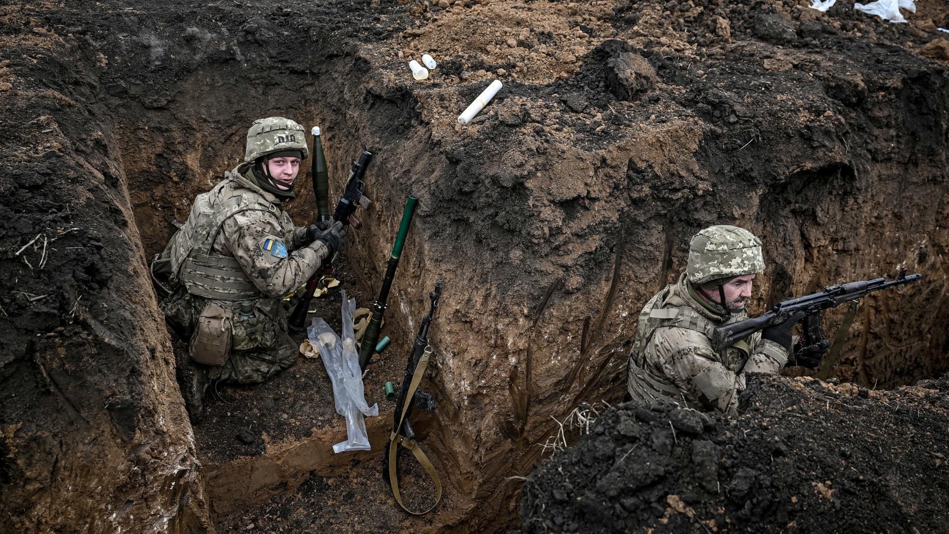 Zwei Soldaten der 110. Territorialverteidigungsbrigade befinden sich in einem Schützengraben in der Region Saporischschja im Südosten der Ukraine. Sie tragen Tarnuniformen, Helme und Schutzwesten. 