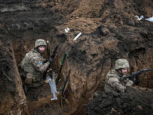 Zwei Soldaten der 110. Territorialverteidigungsbrigade befinden sich in einem Schützengraben in der Region Saporischschja im Südosten der Ukraine. Sie tragen Tarnuniformen, Helme und Schutzwesten. 