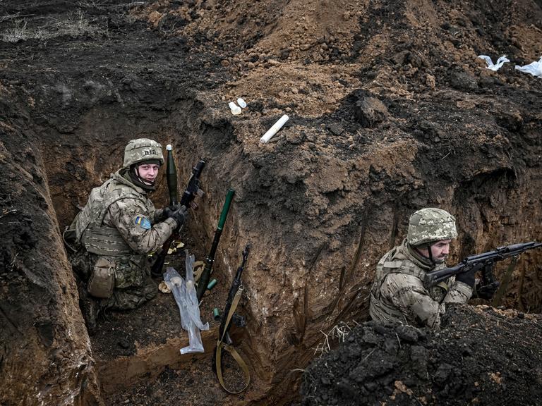 Zwei Soldaten der 110. Territorialverteidigungsbrigade befinden sich in einem Schützengraben in der Region Saporischschja im Südosten der Ukraine. Sie tragen Tarnuniformen, Helme und Schutzwesten. 