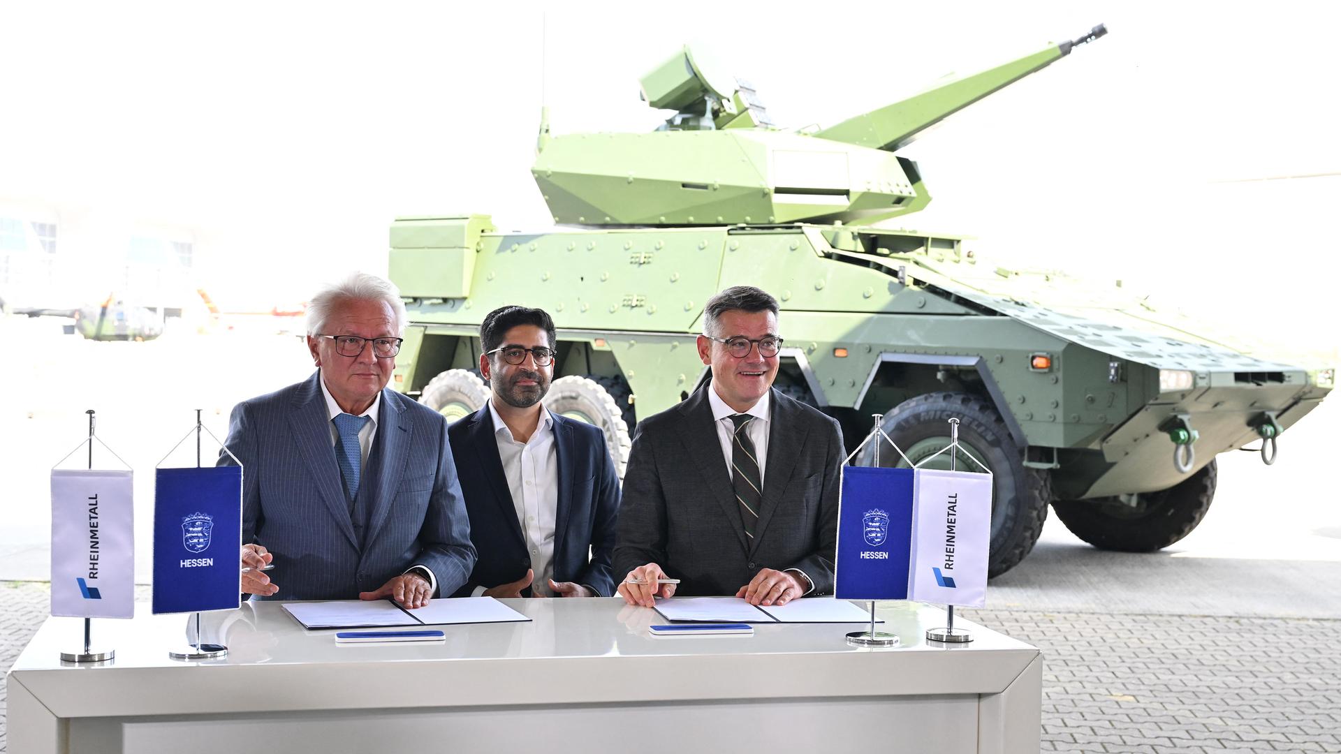 Hessens Ministerpräsident Boris Rhein (r, CDU), Wirtschaftsminister Kaweh Mansoori (M, SPD) und Rheinmetall-Vorstandsvorsitzender Armin Papperger während der Unterzeichnung eines "Memorandum of Understandning" auf dem Flughafen Kassel-Calden. 