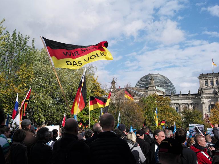 Eine Menschenmenge schwenkt Deutschlandfahnen. Auf einer davon ist zu lesen: "Wir sind das Volk". Im Hintergrund: der Reichstag, Sitz des deutschen Bundestags.