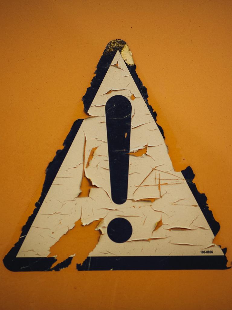 Auf gelbem Hintergrund klebt ein schwarz umrandetes weißes dreieckiges Schild mit einem Ausrufezeichen. Auf gelbem Hintergrund klebt ein schwarz umrandetes weißes dreieckiges Schild mit einem Ausrufezeichen.