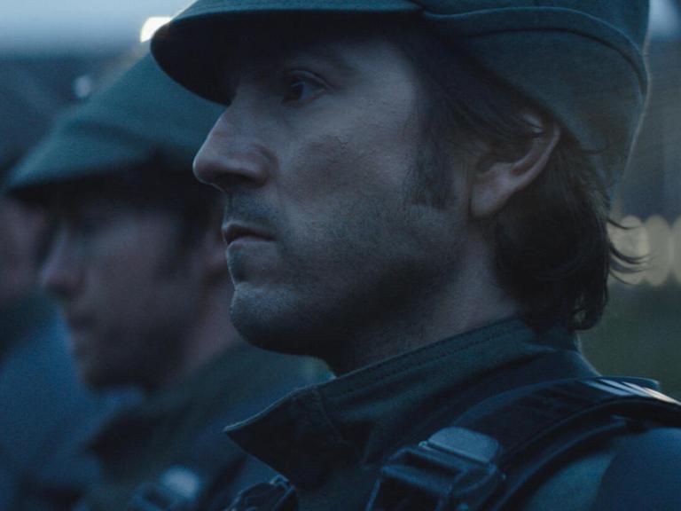 Im Still aus "Andor" ist Diego Luna in einer Großaufnahme im Profil zu sehen. Er scheint gemeinsam mit Soldaten in Reih und Glied zu stehen.