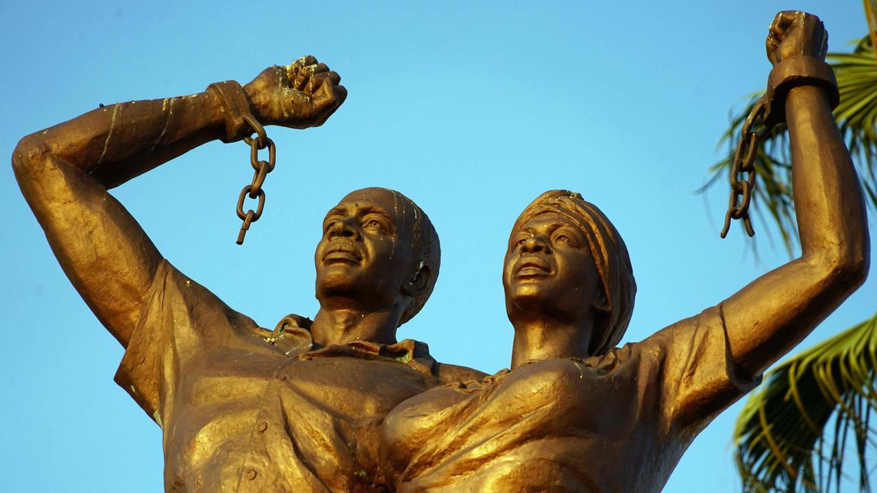 Das riesige Denkmal in Windhoek, Namibia, zeigt einen Mann und eine Frau mit ernstem Gesichtsausdruck, die ihre Arme triumphal gen Himmel strecken. An ihren Handgelenken hängen gesprengte Ketten.