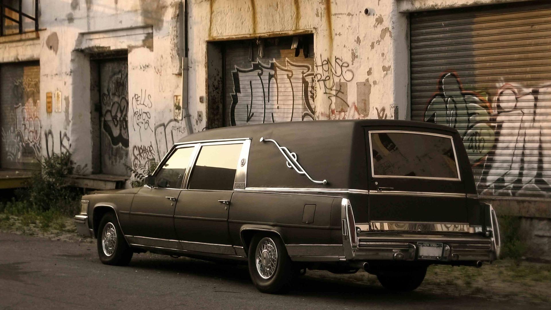Ein Leichenwagen vor einem heruntergekommenen Betonbau. Ein Leichenwagen vor einem heruntergekommenen Betonbau.