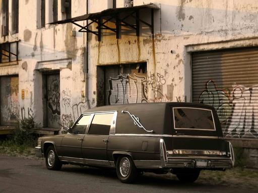 Ein Leichenwagen vor einem heruntergekommenen Betonbau.