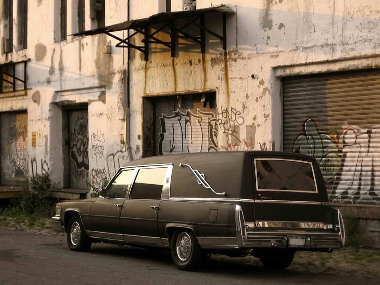 Ein Leichenwagen vor einem heruntergekommenen Betonbau. Ein Leichenwagen vor einem heruntergekommenen Betonbau.
