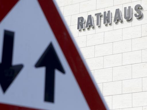 Ein Verkehrsschild mit einem Pfeil nach oben und nach unten ist vor einem Gebäude mit dem Schriftzug "Rathaus" zu sehen.