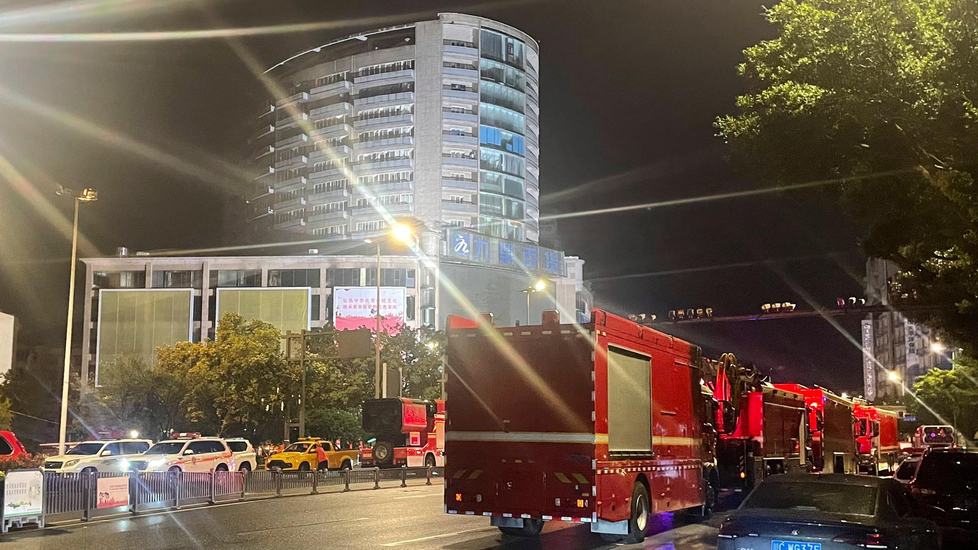 Zu sehen sind Feuerwehrautos und Rettungskräfte, die sich bei Nacht vor einem Hochhaus versammeln.