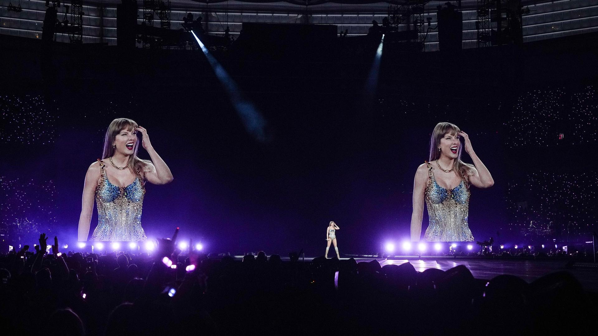 Taylor Swift performed auf der Bühne. Hinter ihr sieht man sie zwei Mal riesengroß auf Leinwänden. Im Vordergrund steht Publikum. Taylor Swift performed auf der Bühne. Hinter ihr sieht man sie zwei Mal riesengroß auf Leinwänden. Im Vordergrund steht Publikum.