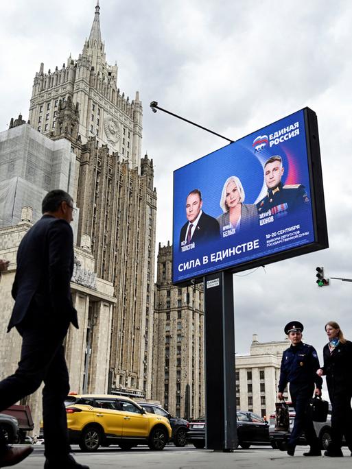 Fußgänger in Moskau gehen am Gebäude des russischen Außenministeriums und an einem Wahlplakat für die Wahl zur russischen Staatsduma (Unterhaus des russischen Parlaments) vorbei.