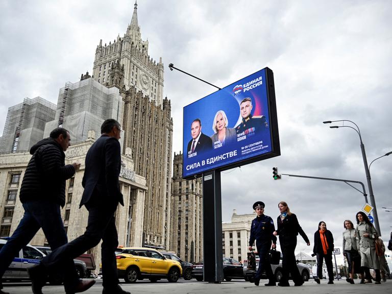 Fußgänger in Moskau gehen am Gebäude des russischen Außenministeriums und an einem Wahlplakat für die Wahl zur russischen Staatsduma (Unterhaus des russischen Parlaments) vorbei.