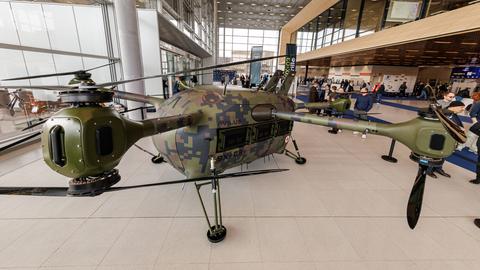 Die Grille ist eine elektrisch betriebene Rettungsdrohne. Der Multikopter soll verwundete Soldaten aus Kampfgebieten evakuieren können. Sie wird auf einer Messe präsentiert. Im Hintergrund der Messehalle das Publikum.
