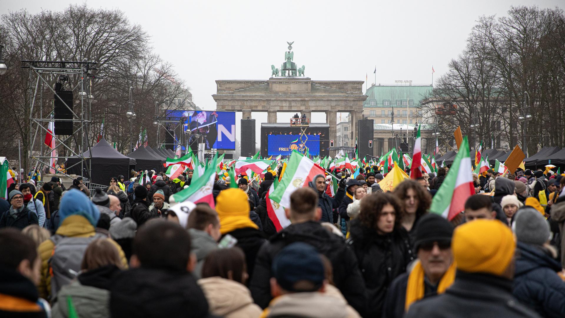 Eine große Menschenmenge steht vor dem Brandenburger Tor. Sie tragen iranische Flaggen in rot, weiß und grün.