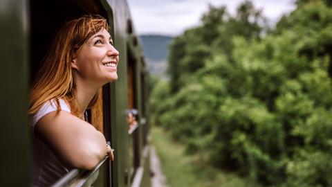 Eine Frau fährt während des Bahnfahrens aus dem Fenster. Der Zug fährt durch eine grüne Landschaft