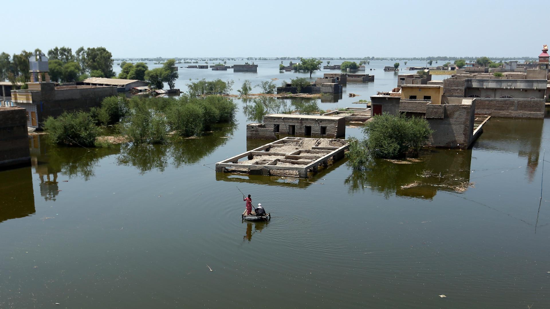 Menschen benutzen ein behelfsmäßiges Floß, um sich in den Fluten des Monsuns zurechtzufinden, im Distrikt Dadu in der Provinz Sindh in Pakistan. Sie fahren damit durch die Fluten von einem Haus zum anderen.