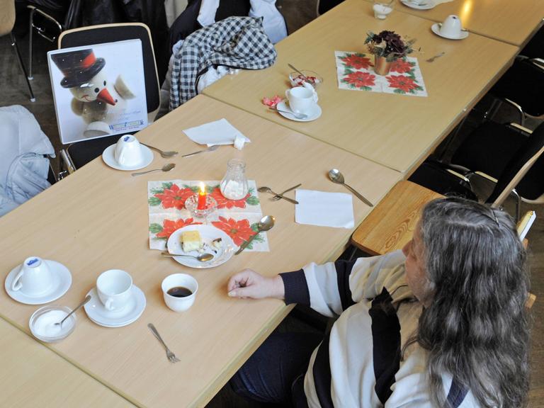 Eine Bedürftige sitzt auf einem Stuhl gegenüber einem BIld von einem Schneemann. Sie isst Käsekuchen.