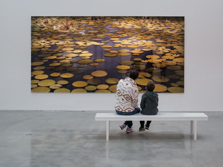 Eine Mutter sitzt mit ihrem Sohn im Israel Museum vor einer großen Fotografie eines Seerosenteichs. 
