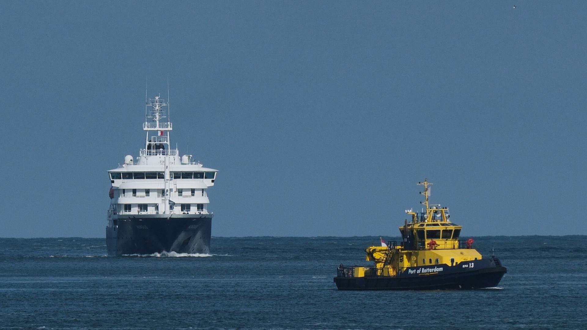 Das Kreuzfahrtschiff "Hondius" und ein Lotsenschiff im dunkelblauen Meer unter blauem Himmel. Das Kreuzfahrtschiff "Hondius" und ein Lotsenschiff im dunkelblauen Meer unter blauem Himmel.