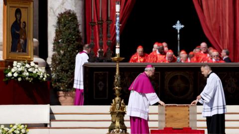 Ein Erzbischof steht bei der Trauermesse für den verstorbenen Papst Franziskus auf dem Petersplatz neben dem verschlossenen Sarg.