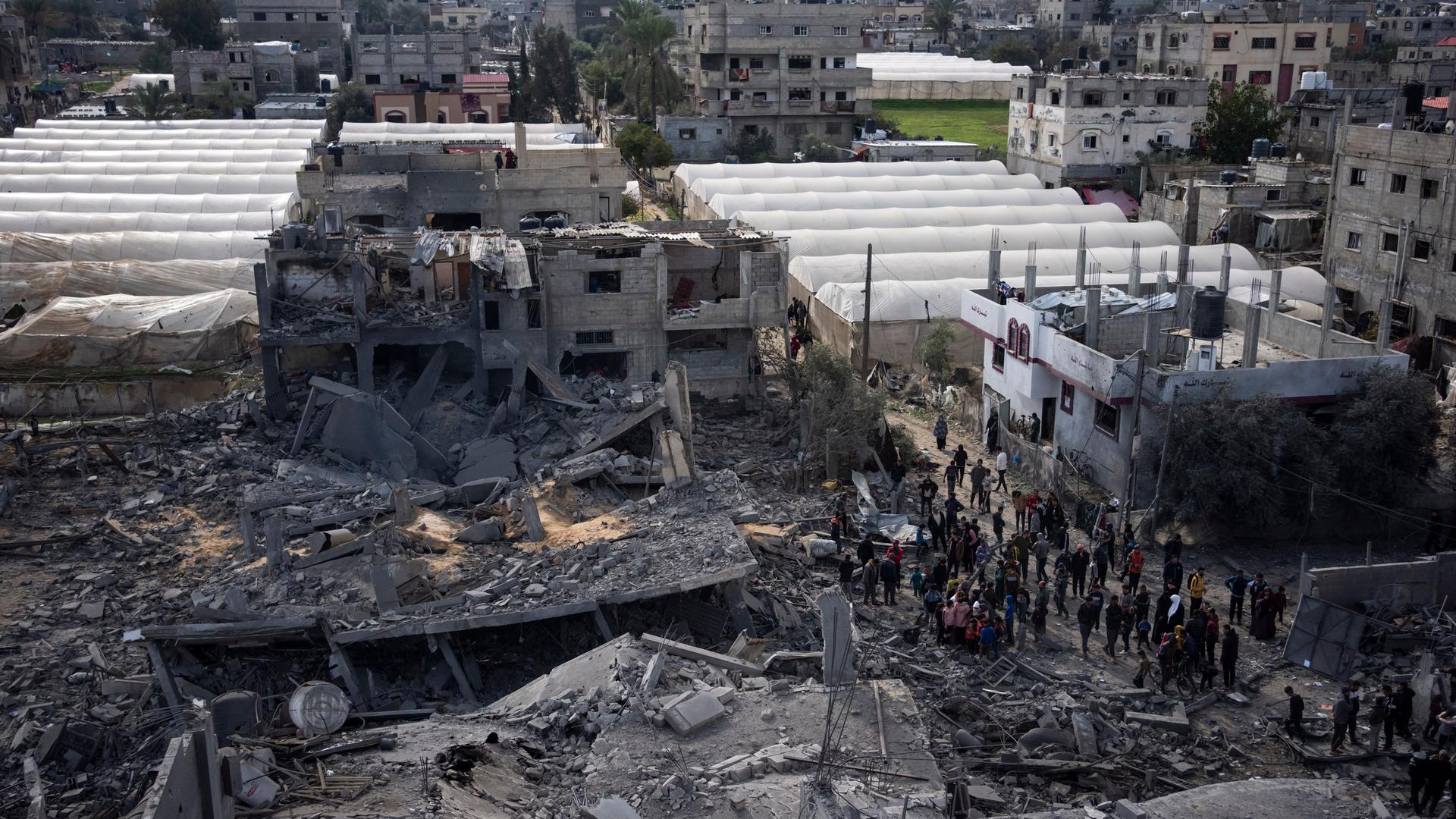 Zahlreiche Palästinenser stehen vor zerstörten Gebäuden in Rafah - im Hintergrund sind weiße Zeltreihen zu sehen.