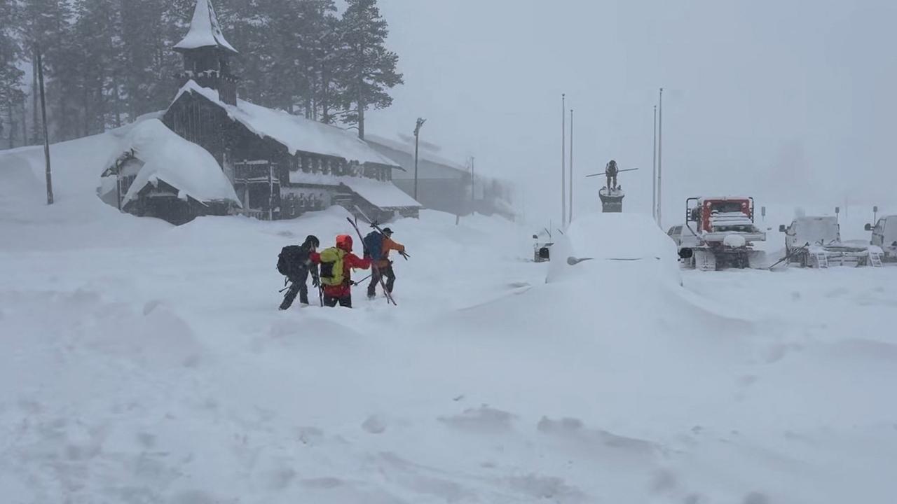 Rettungskräfte stapfen durch hohen Schnee an einem Gebäude und mehreren Fahrzeugen vorbei. Rettungskräfte stapfen durch hohen Schnee an einem Gebäude und mehreren Fahrzeugen vorbei.