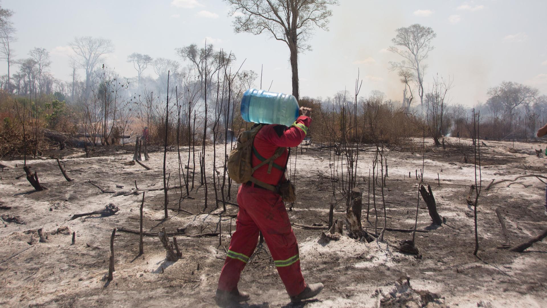 Ein Mitglied der Feuerwehr trägt ein Wasserkanister bei einem Einsatz an einem verbrannten Feld im Osten von Bolivien in der Region Chiquitania.