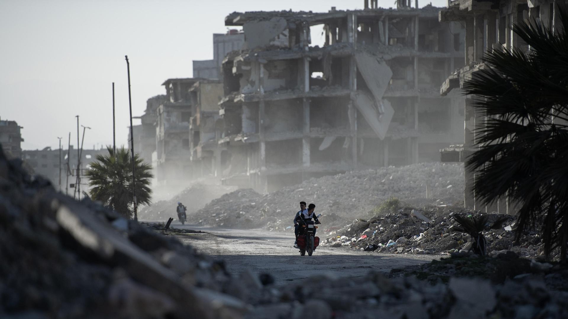  Zwei junge Menschen fahren auf einem Motorrad zwischen den zerstörten Gebäuden hindurch, während die Syrer im Lager Yarmouk in Damaskus ihrem Alltag nachgehen. 