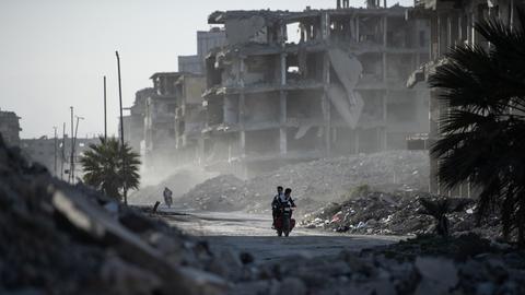 Zwei junge Menschen fahren auf einem Motorrad zwischen den zerstörten Gebäuden hindurch, während die Syrer im Lager Yarmouk in Damaskus ihrem Alltag nachgehen. Zwei junge Menschen fahren auf einem Motorrad zwischen den zerstörten Gebäuden hindurch, während die Syrer im Lager Yarmouk in Damaskus ihrem Alltag nachgehen.