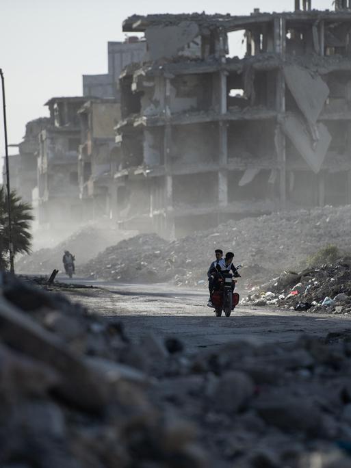  Zwei junge Menschen fahren auf einem Motorrad zwischen den zerstörten Gebäuden hindurch, während die Syrer im Lager Yarmouk in Damaskus ihrem Alltag nachgehen. 