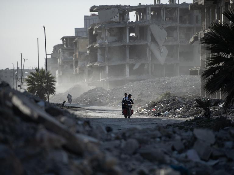  Zwei junge Menschen fahren auf einem Motorrad zwischen den zerstörten Gebäuden hindurch, während die Syrer im Lager Yarmouk in Damaskus ihrem Alltag nachgehen. 