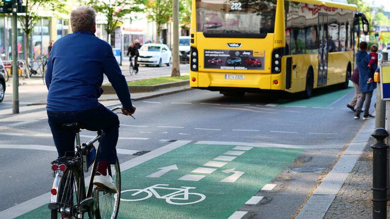 Ein Mann fährt mit seinem Fahrrad auf einem grün markierten Radweg auf der Schlossstrasse in Steglitz. Links vor ihm fährt ein gelber Bus.