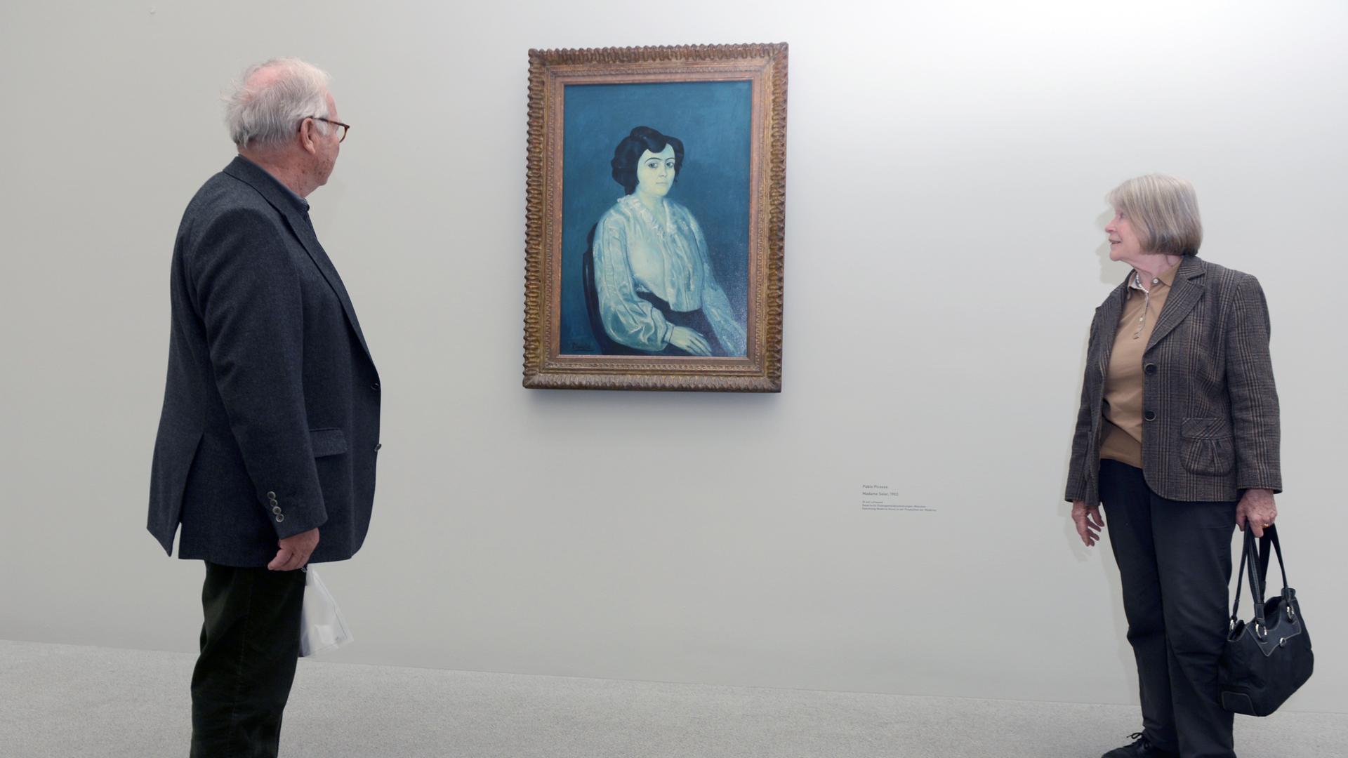 Zwei Besucher betrachten in einer Ausstellung das Gemälde "Madame Soler" (1903) von Pablo Picasso.