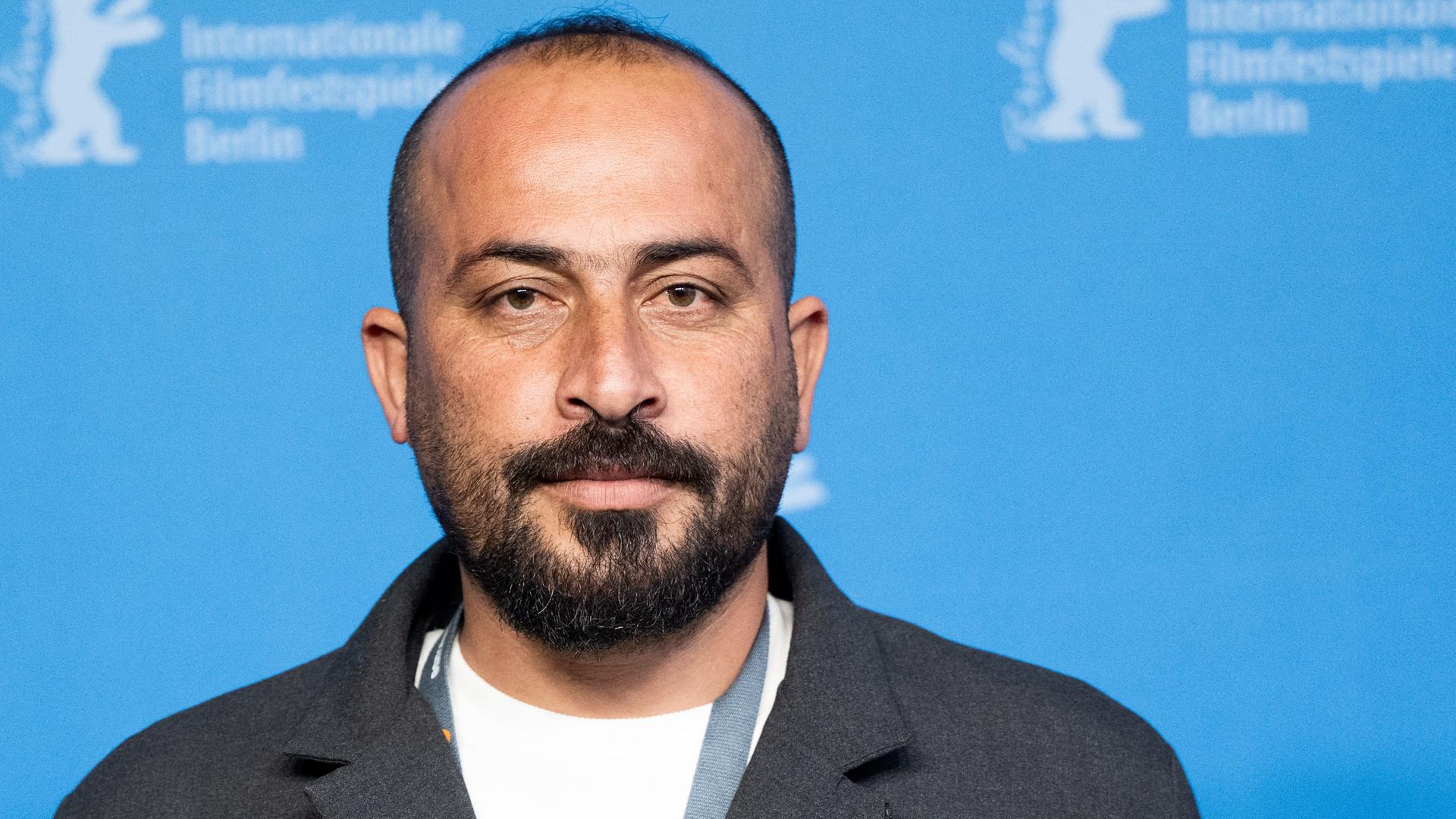 Der Regisseur Hamdan Ballal steht vor einer blauen Wand. Am oberen Rand der Wand erkennt man das Berlinale-Zeichen. 