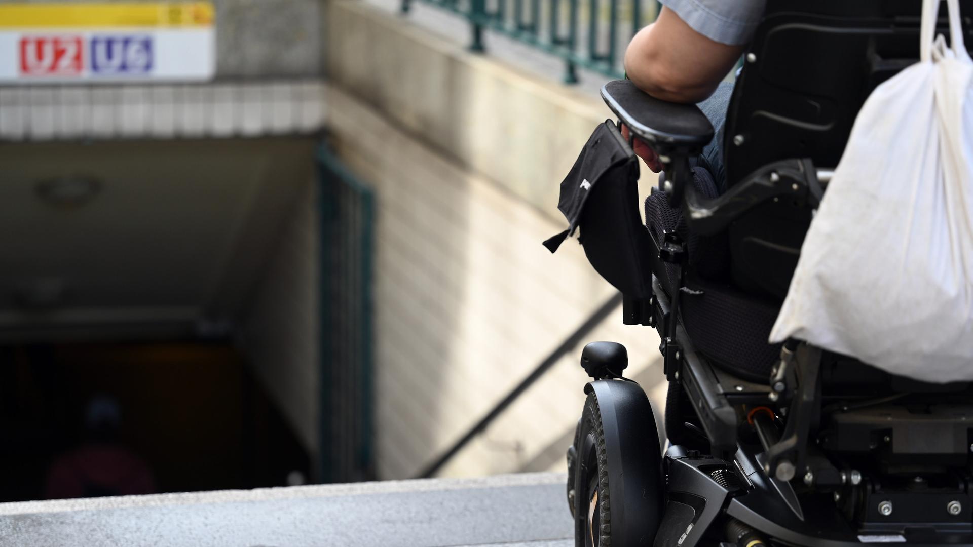 Ein Mann steht mit seinem Rollstuhl vor der Treppe eines Eingangs zur U-Bahn. 