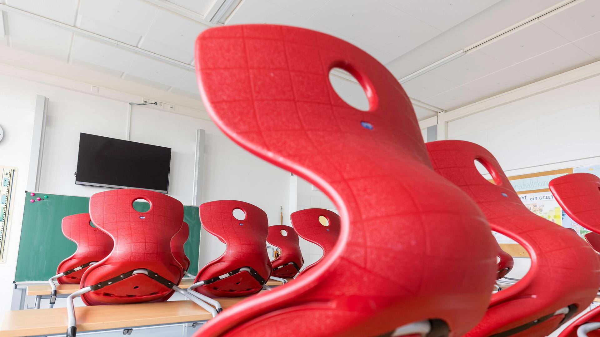 Ein Klassenraum in einer Dresdner Schule: Die roten Stühle sind auf die Tische gestellt. Im Vordergrund ist eine Tafel und ein Bildschirm, der an der Wand hängt.