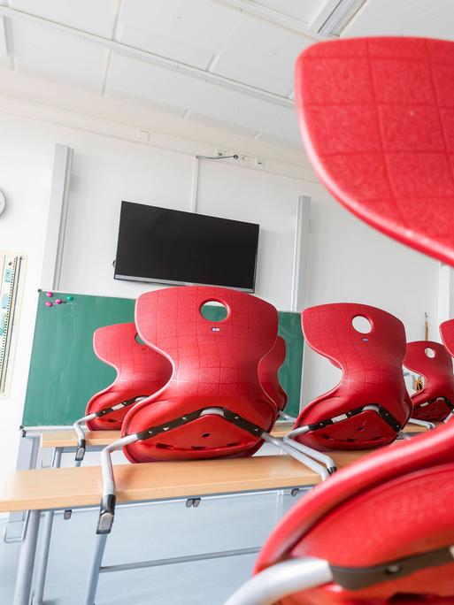Ein Klassenraum in einer Dresdner Schule: Die roten Stühle sind auf die Tische gestellt. Im Vordergrund ist eine Tafel und ein Bildschirm, der an der Wand hängt. 