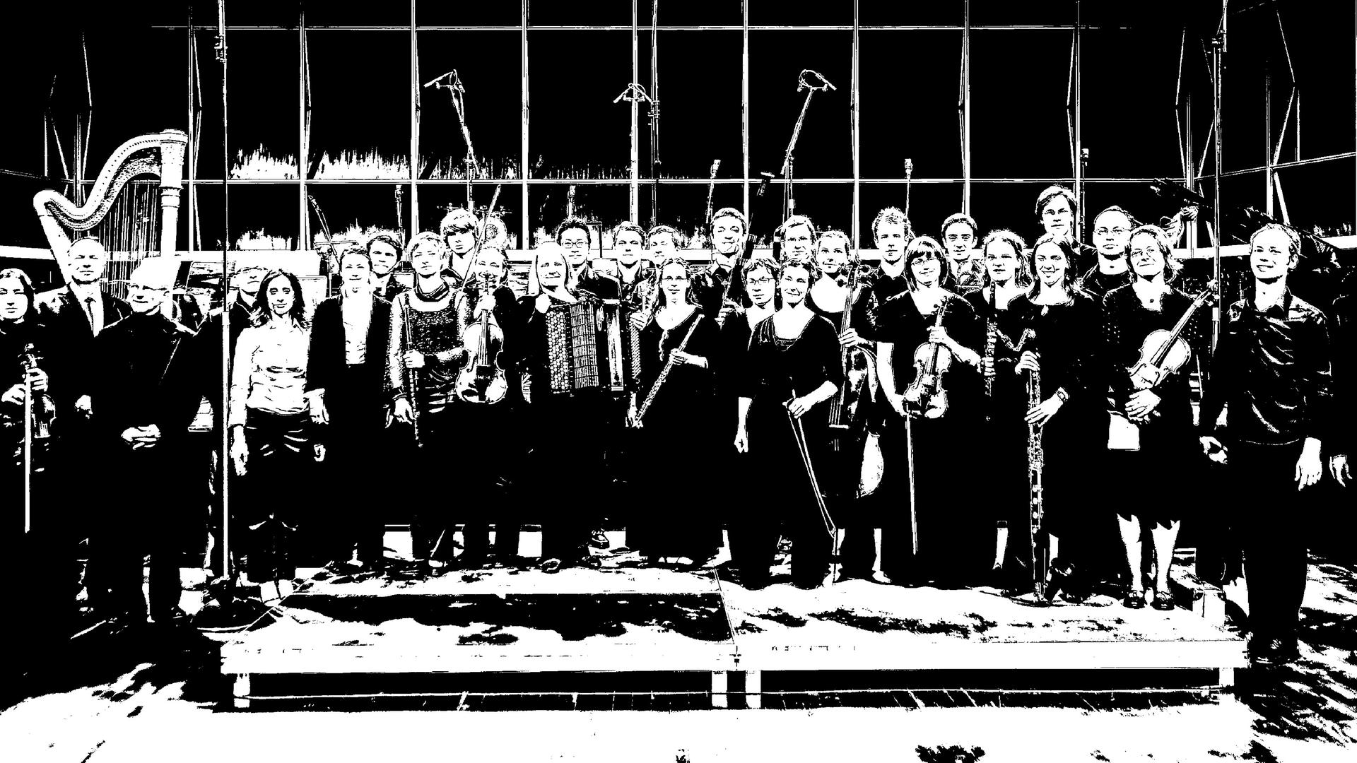 Das Ensemble steht mit seinen Instrumenten auf der Bühne und lacht auf einem schwarz-weiß-Foto. Das Ensemble steht mit seinen Instrumenten auf der Bühne und lacht auf einem schwarz-weiß-Foto.