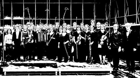 Das Ensemble steht mit seinen Instrumenten auf der Bühne und lacht auf einem schwarz-weiß-Foto.