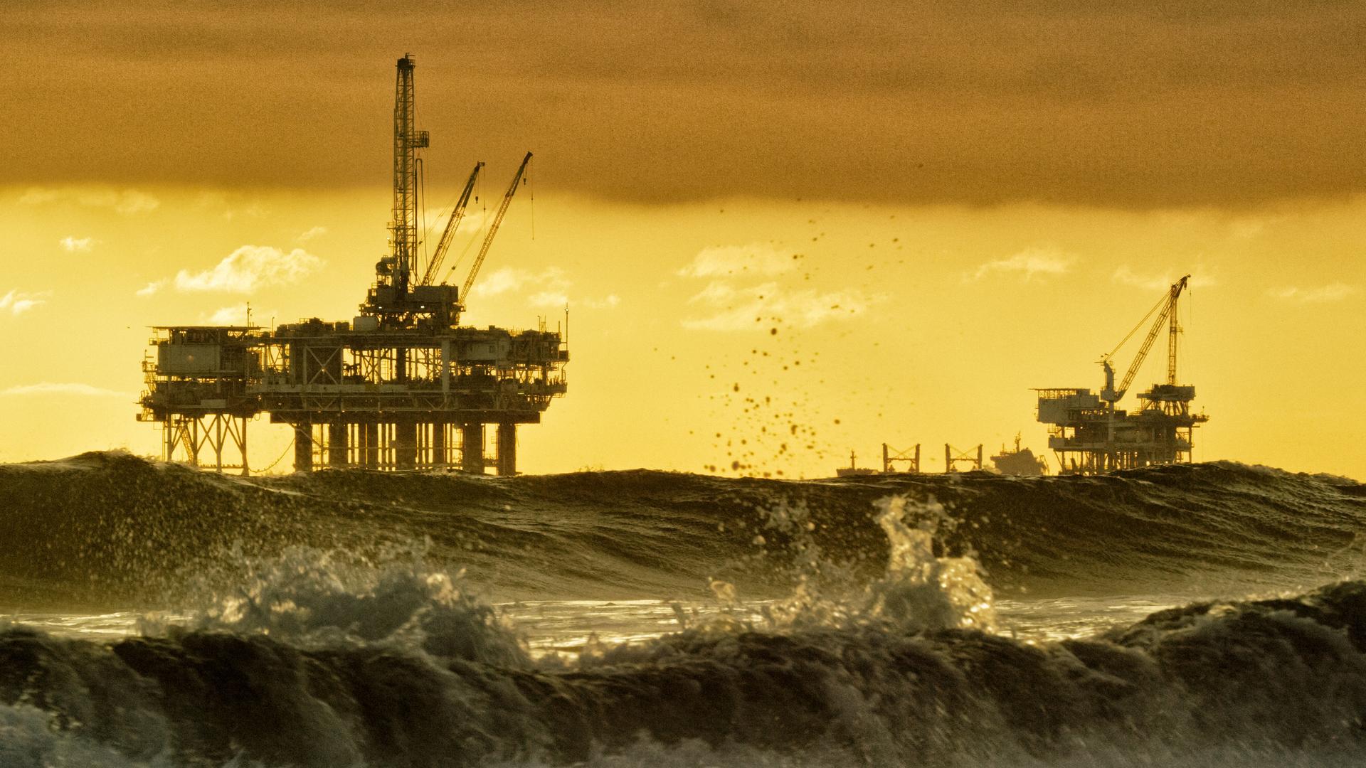 Starke Wellen brechen in der Nähe von Huntington Beach in Südkalifornien, mit mehreren Silhouetten von Offshore-Ölbohrplattformen und einem Öltanker am Horizont in der Ferne bei Sonnenuntergang unter einem dramatischen, stürmischen Himmel. Starke Wellen brechen in der Nähe von Huntington Beach in Südkalifornien, mit mehreren Silhouetten von Offshore-Ölbohrplattformen und einem Öltanker am Horizont in der Ferne bei Sonnenuntergang unter einem dramatischen, stürmischen Himmel.