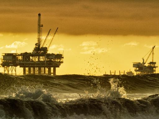 Starke Wellen brechen in der Nähe von Huntington Beach in Südkalifornien, mit mehreren Silhouetten von Offshore-Ölbohrplattformen und einem Öltanker am Horizont in der Ferne bei Sonnenuntergang unter einem dramatischen, stürmischen Himmel. Starke Wellen brechen in der Nähe von Huntington Beach in Südkalifornien, mit mehreren Silhouetten von Offshore-Ölbohrplattformen und einem Öltanker am Horizont in der Ferne bei Sonnenuntergang unter einem dramatischen, stürmischen Himmel.