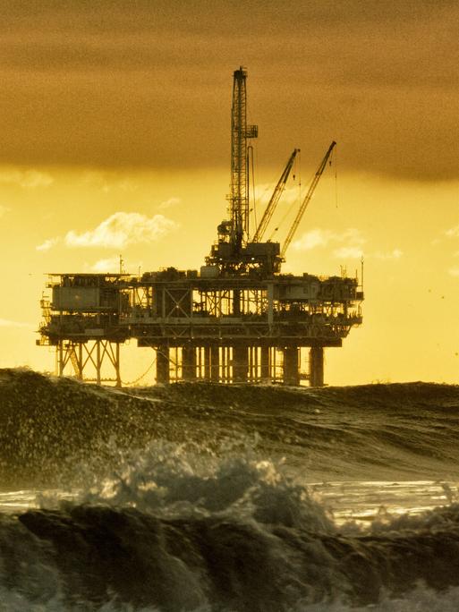 Starke Wellen brechen in der Nähe von Huntington Beach in Südkalifornien, mit mehreren Silhouetten von Offshore-Ölbohrplattformen und einem Öltanker am Horizont in der Ferne bei Sonnenuntergang unter einem dramatischen, stürmischen Himmel. Starke Wellen brechen in der Nähe von Huntington Beach in Südkalifornien, mit mehreren Silhouetten von Offshore-Ölbohrplattformen und einem Öltanker am Horizont in der Ferne bei Sonnenuntergang unter einem dramatischen, stürmischen Himmel.